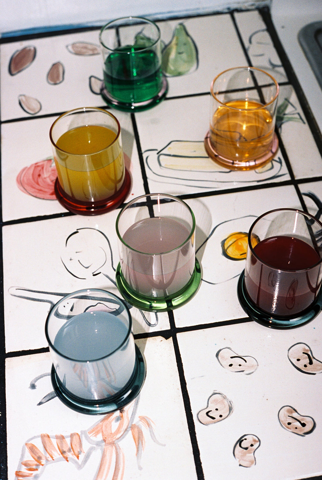 Sophie Lou Jacobsen Fritter tumblers with colored drinks arranged on a hand-painted tile counter.