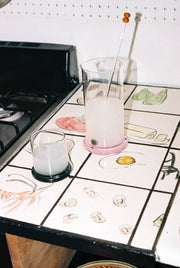 Glass pitcher and tumbler with milky drink on illustrated kitchen tile counter by stove