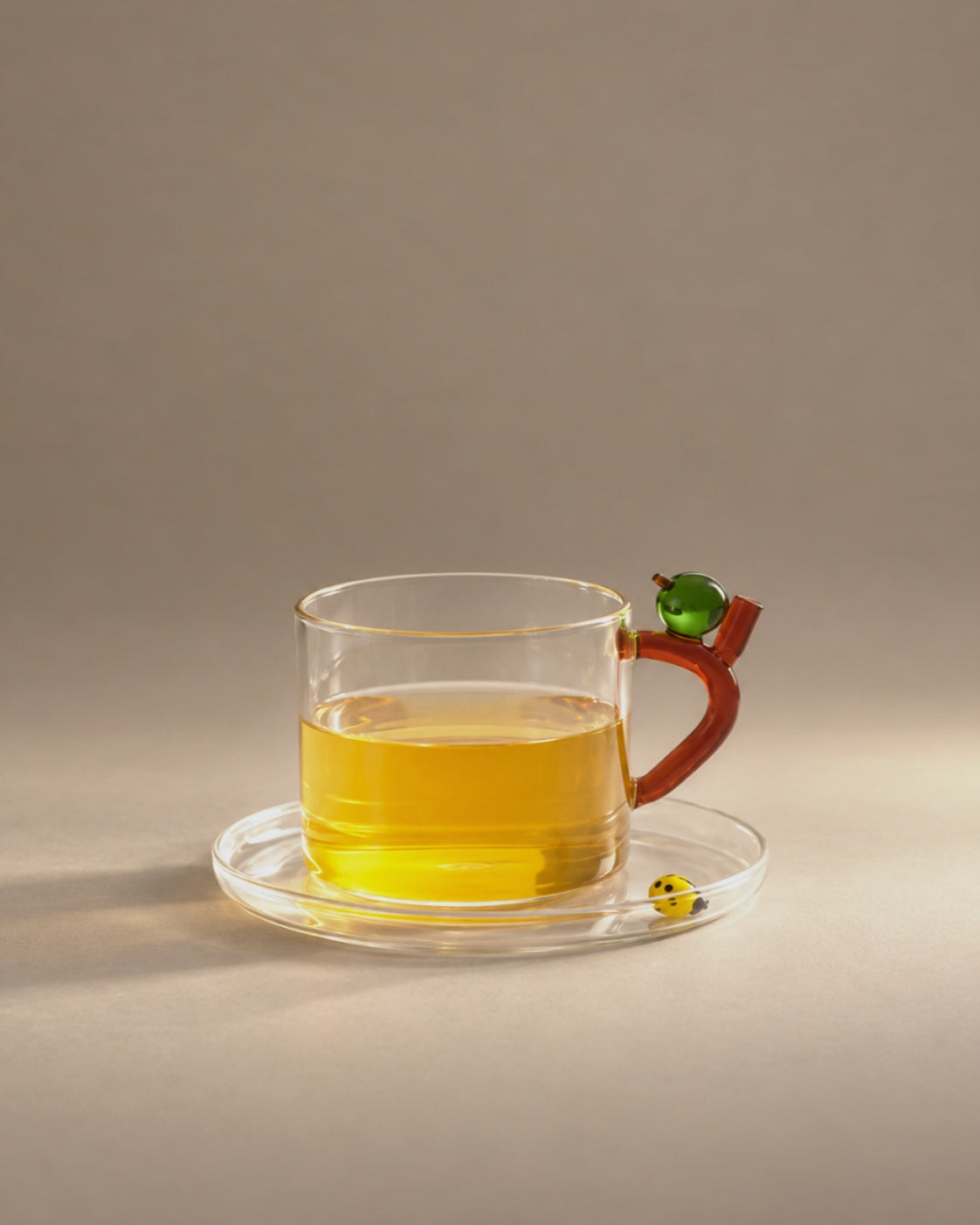 Ladybug Apple Tea Cup with tea, a red handle with a small green apple and a yellow ladybug on the saucer, photographed in the Son of Rand studio