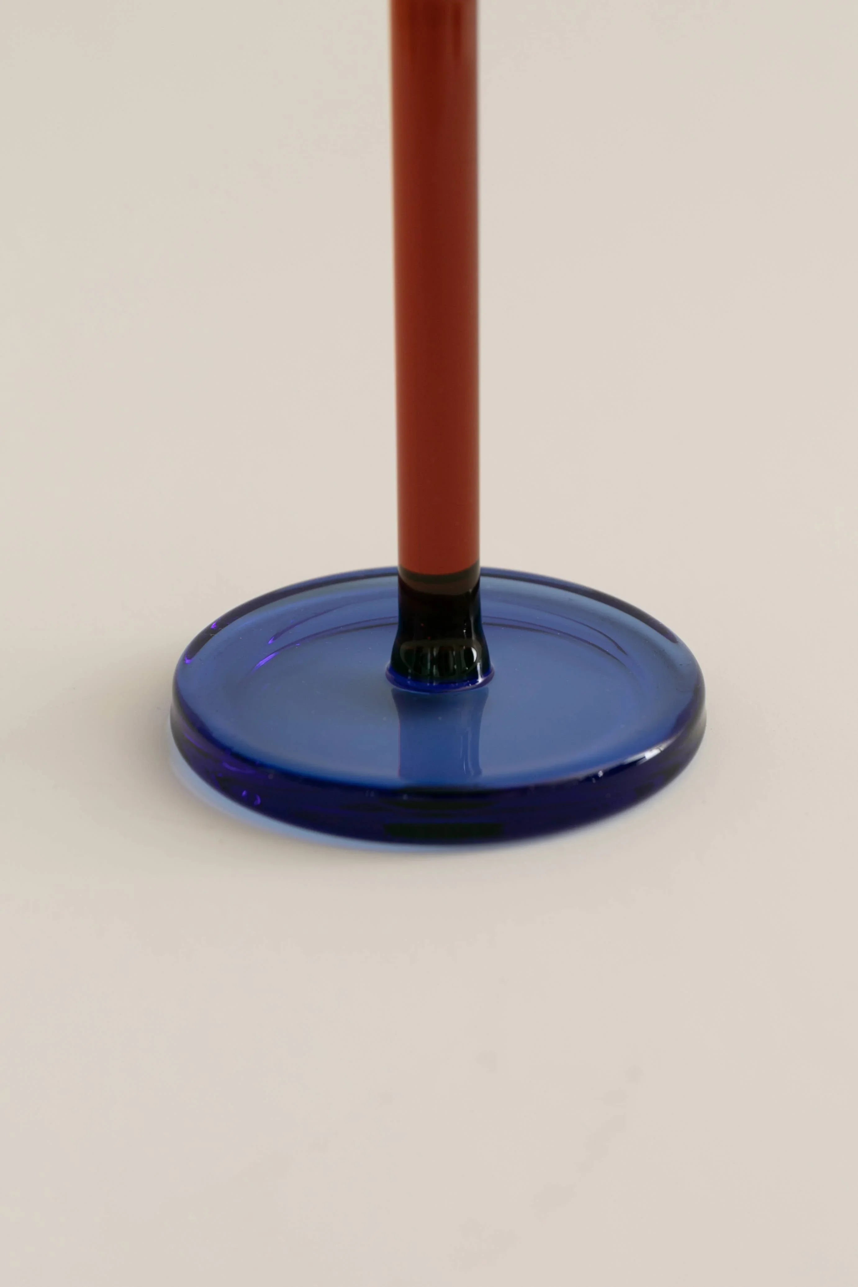 Close-up of blue glass base with red stem on light background