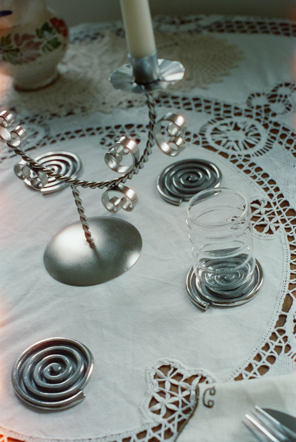 Spiral metal coasters, glass, and silver candle holder on lace tablecloth
