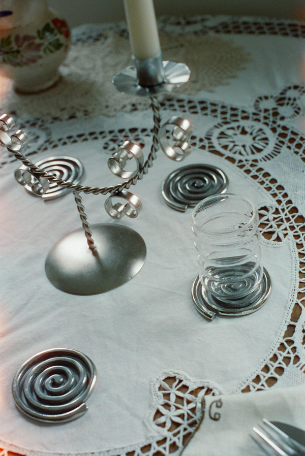 Spiral metal coasters, glass, and silver candle holder on lace tablecloth