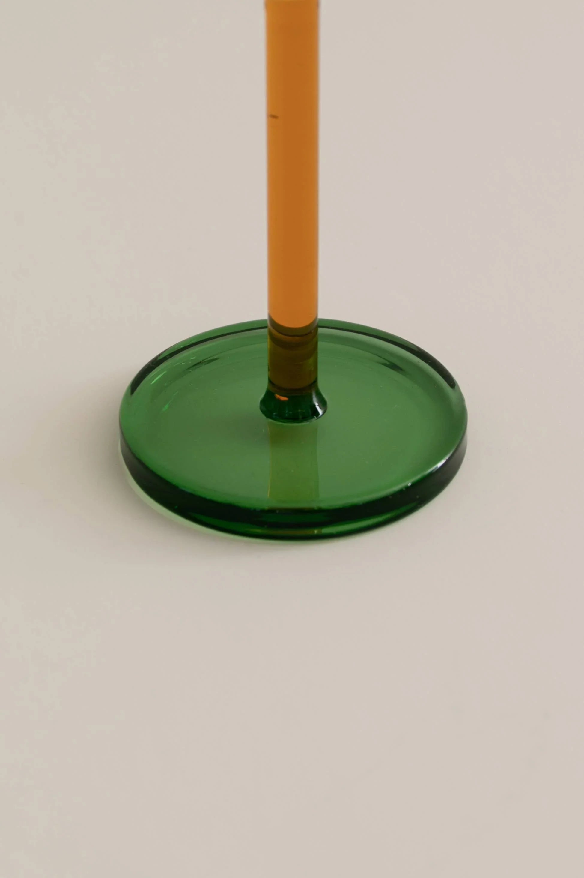 Close-up of a glass with an orange stem and a green round base on a light background.