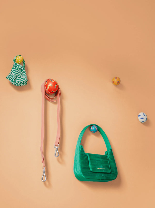 Colorful Chiaozza wall hooks on peach background with hanging green bag and strap