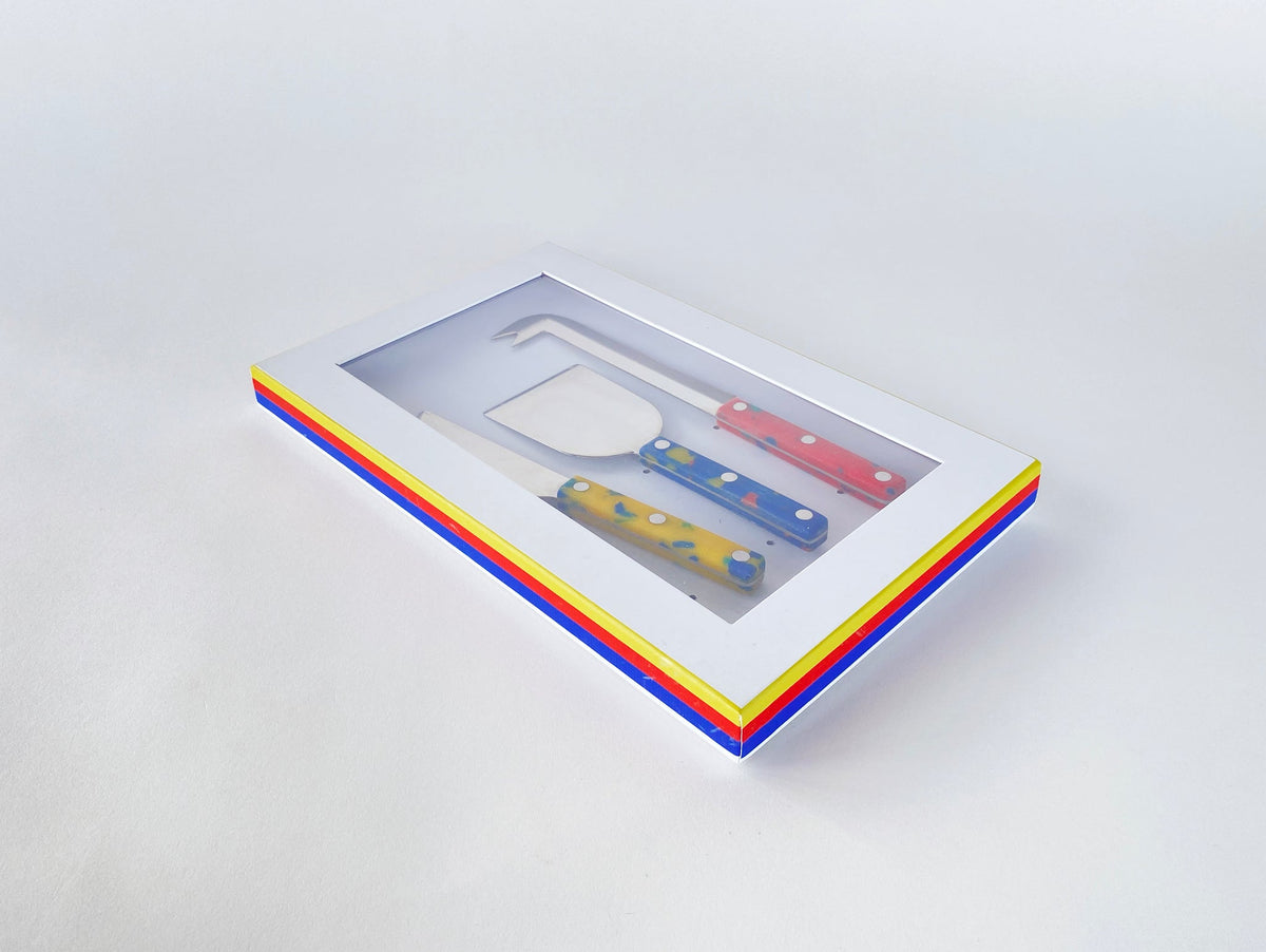 Cheese knife set in a white presentation box with red, yellow, and blue striped edges