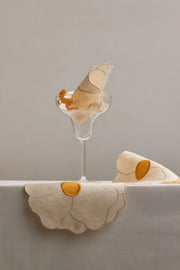 Embroidered linen flower napkins with yellow centers in a glass on a white table.