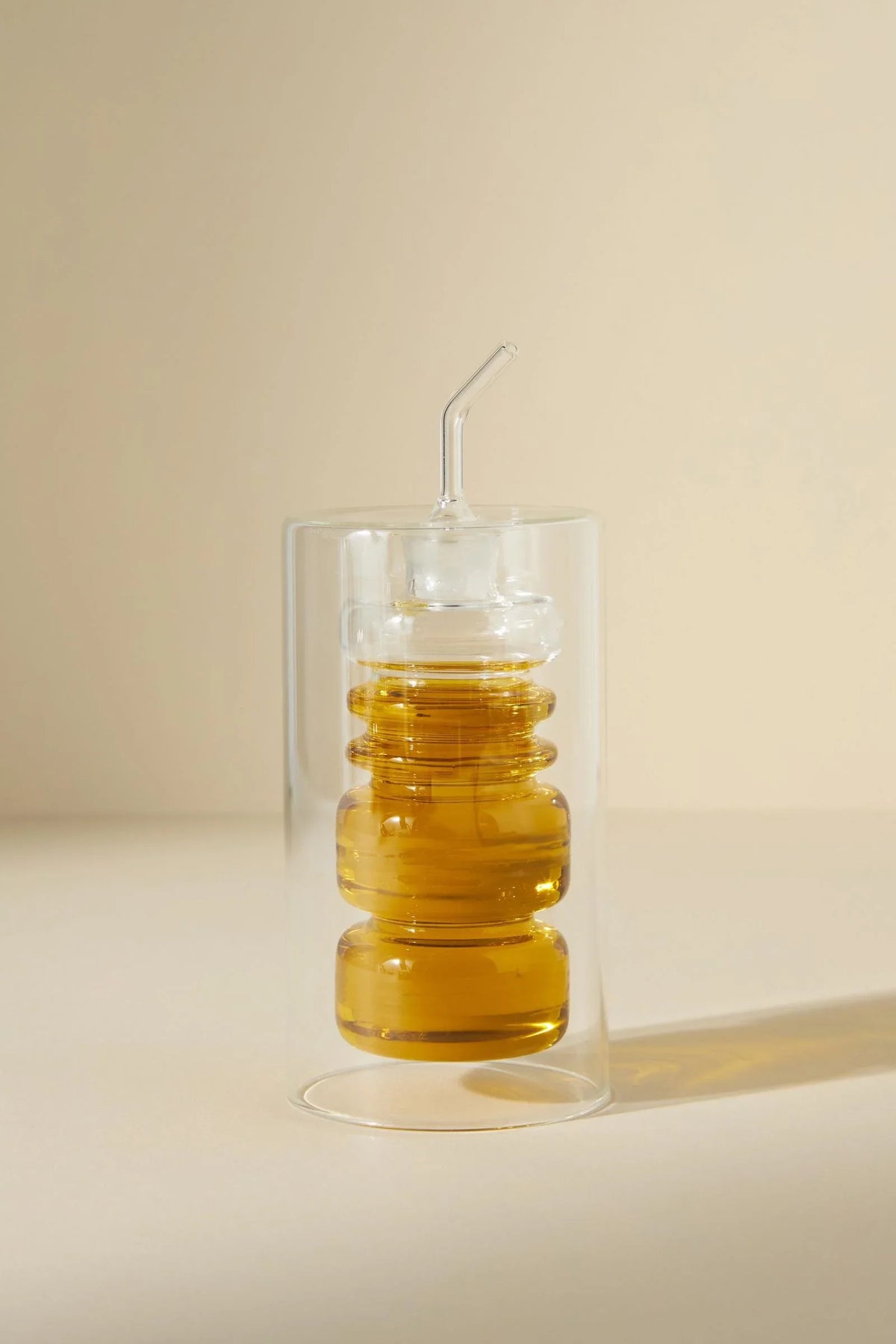 Modern clear glass honey jar with dipper, filled with honey on beige background