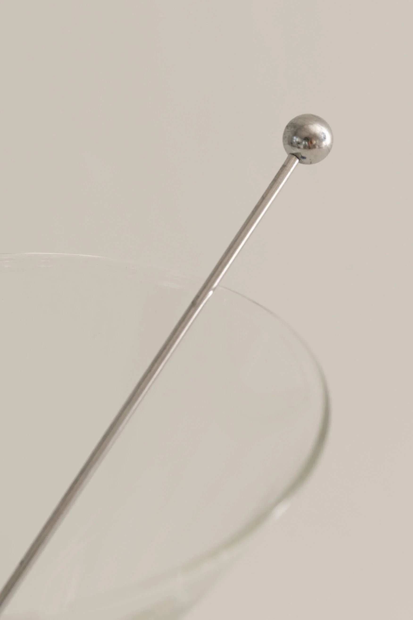 Stainless steel cocktail stirrer with round end in a clear glass on neutral background