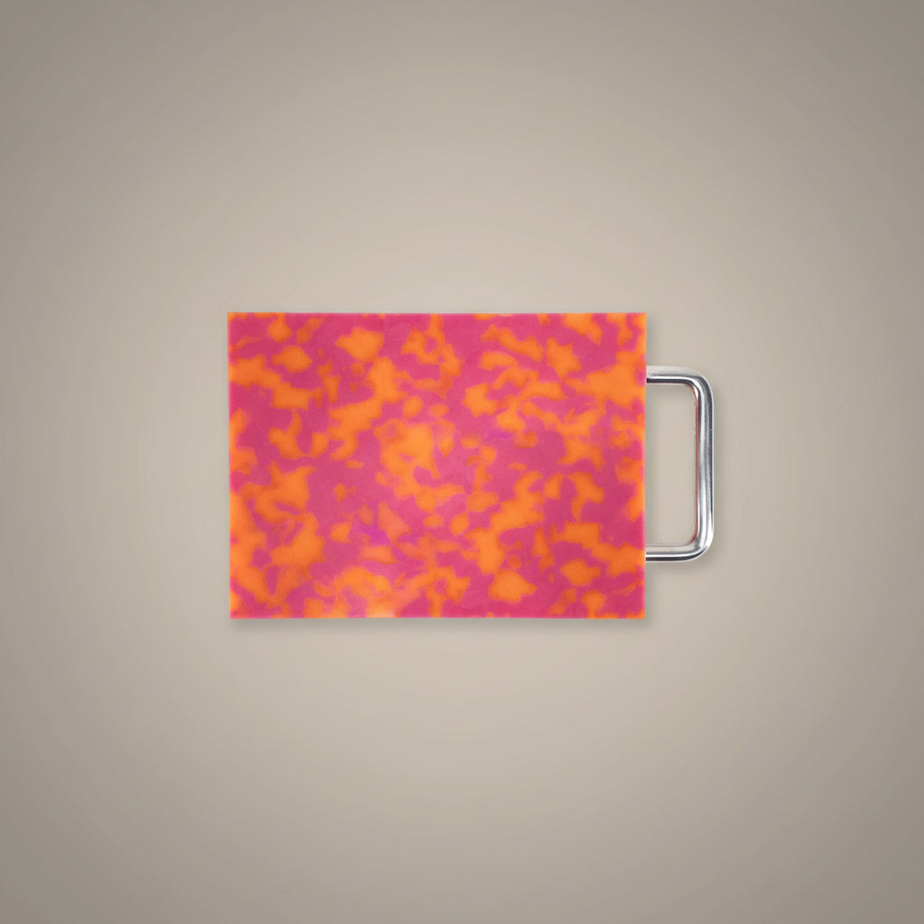 Small pink and orange marbled cutting board with chrome handle on white background