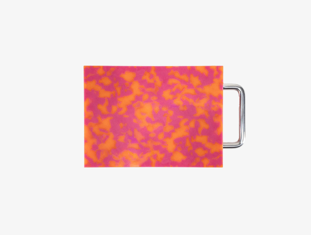 Small pink and orange marbled cutting board with chrome handle on white background