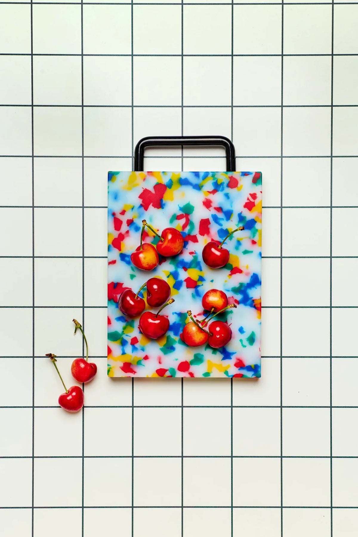 Cherries on colorful terrazzo cutting board with handle on white grid background