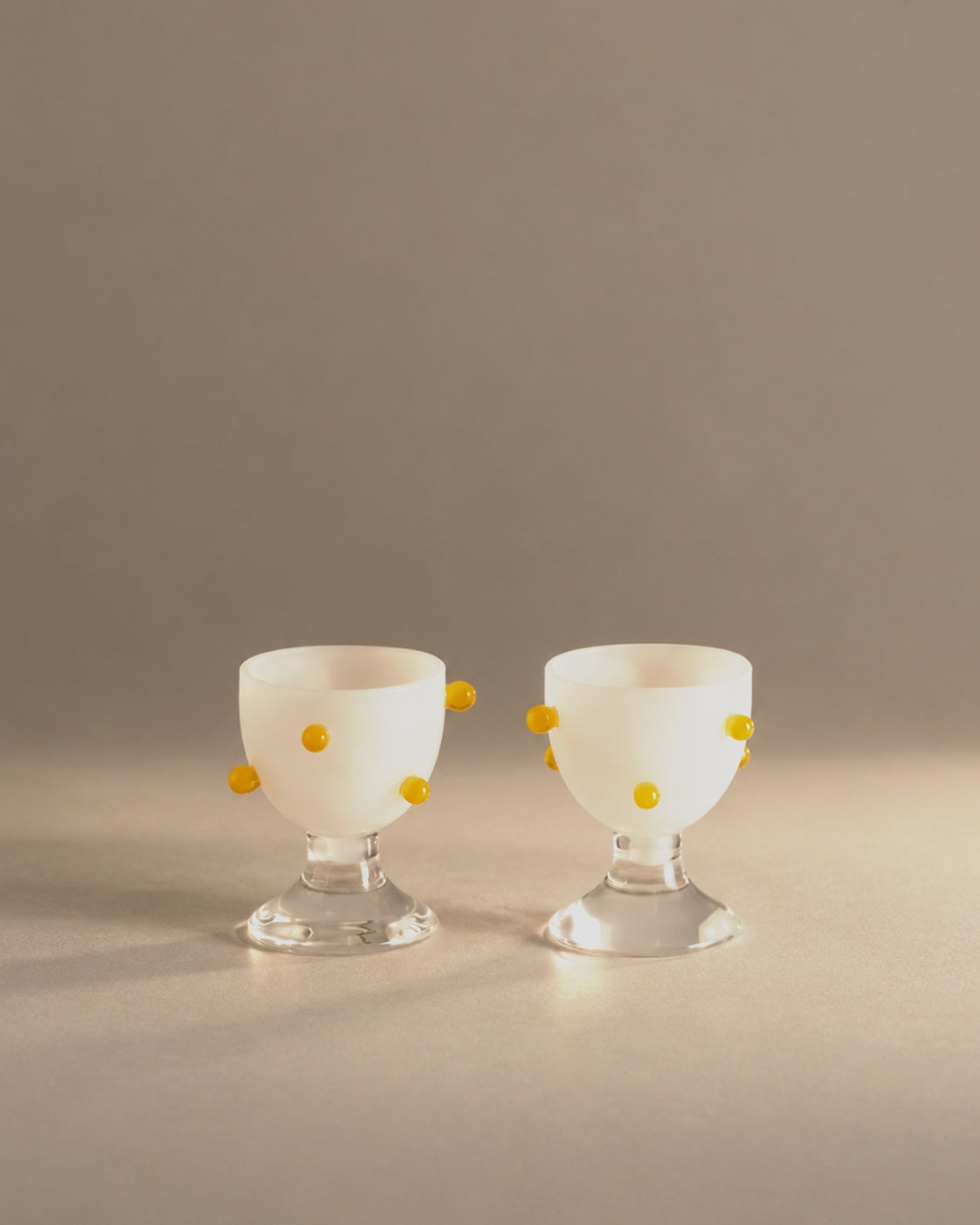 Pomponette Egg Cups, a pair of frosted white glass cups with golden droplets, photographed in the Son of Rand studio