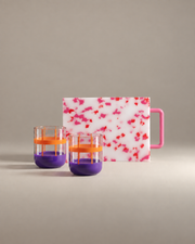 The Host Gift Set: two orange and lilac banded glass tumblers in front of a pink confetti mini cutting board