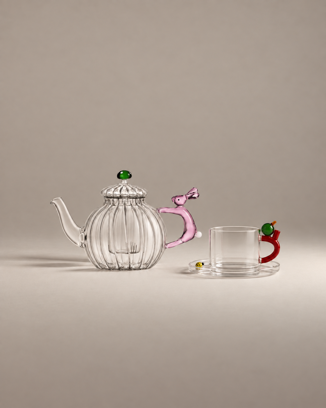The Tea Party Gift Set: a clear ribbed glass teapot with a pink rabbit handle and a glass tea cup with a yellow ladybug on the saucer