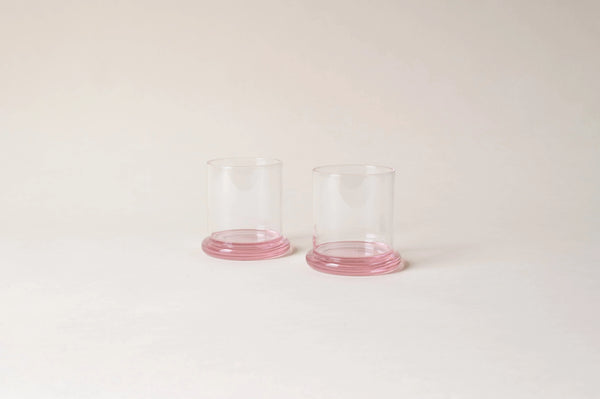 Pair of clear glass tumblers with pink bases on a light background