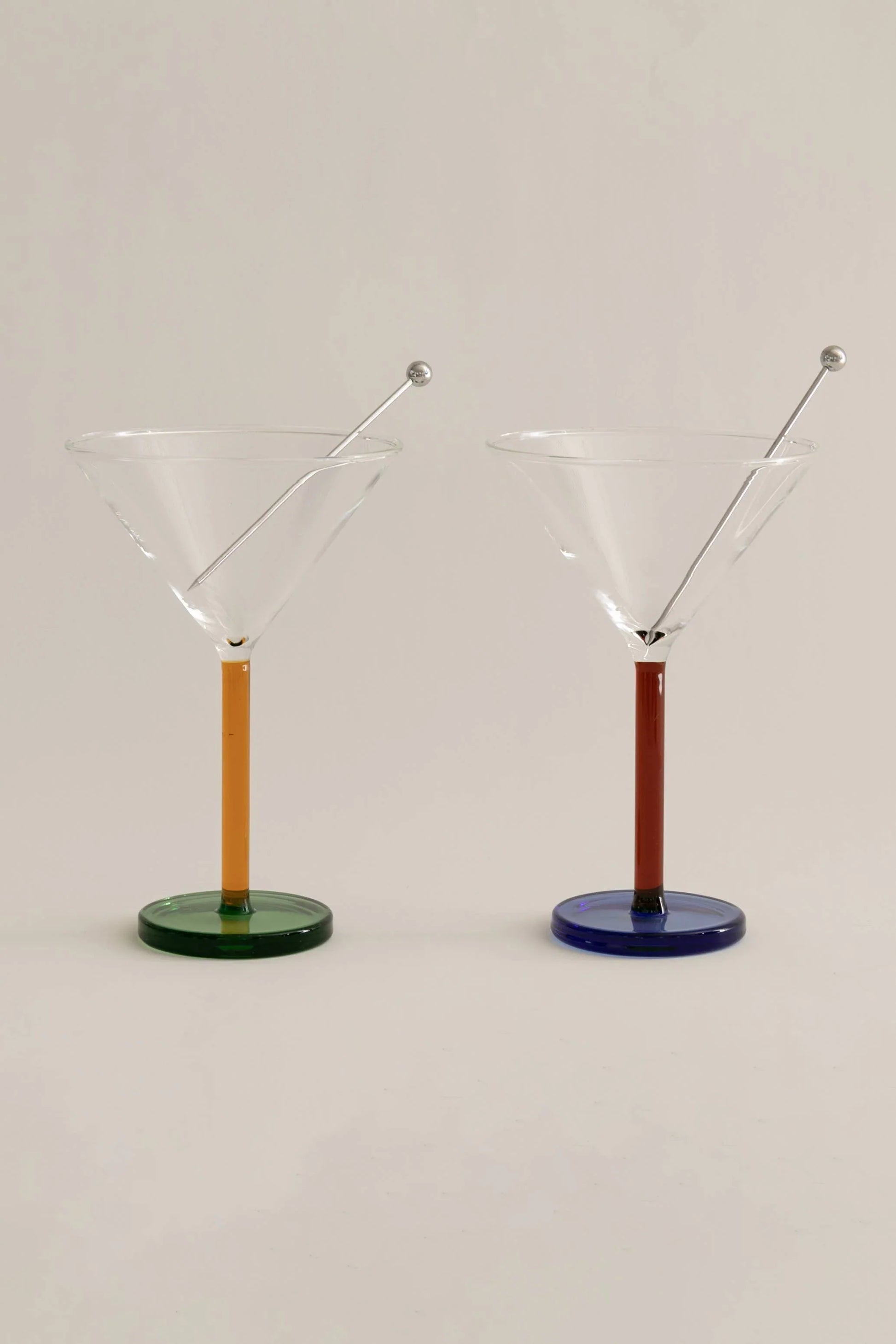 Two colored stem martini glasses with cocktail picks on white background