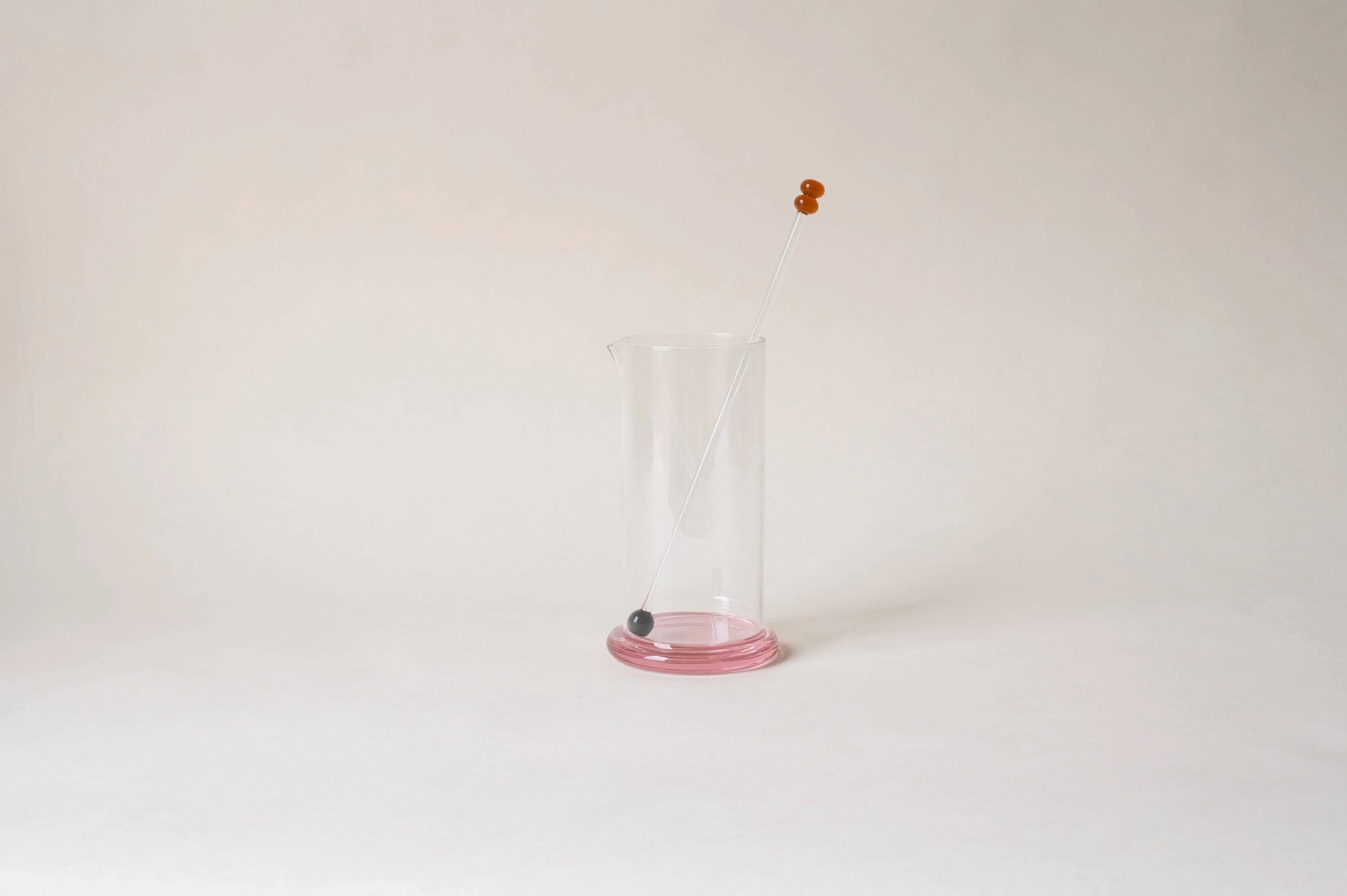 Clear glass beaker with pink base and glass stirrer on white background